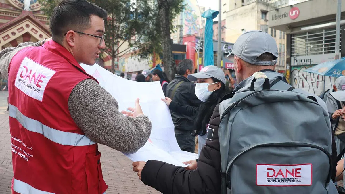 Dos Censistas del DANE, uno con chaleco rojo y otro con gorra y mochila, revisando un mapa o plano en la calle